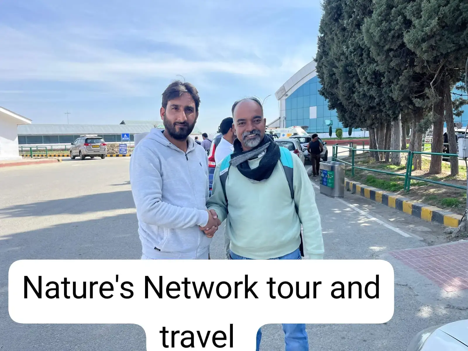 Two men shaking hands outside a travel office, with Nature's Network Tour and Travel branding visible.